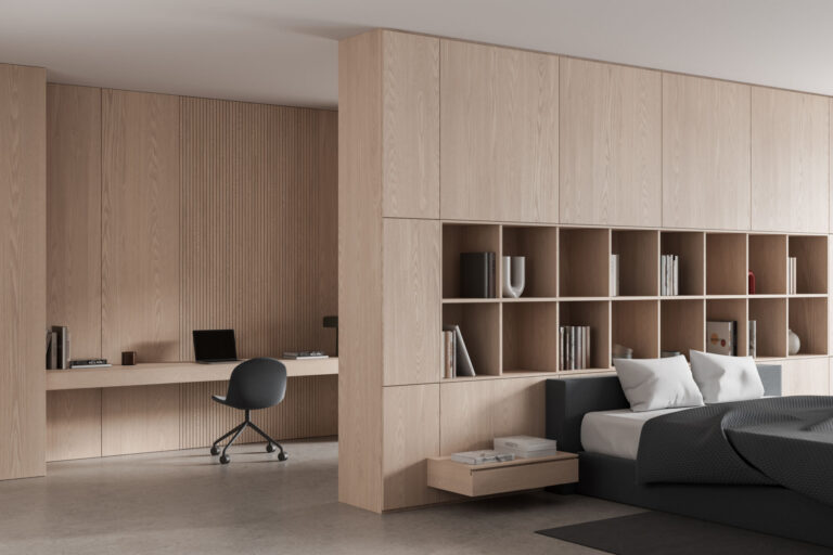 A minimalist bedroom with a built-in wooden desk and shelving unit, featuring a laptop, chair, and a bed with white pillows and a dark grey duvet. White oak wall panels from composite panels and decorative surfaces. Wall panel trend