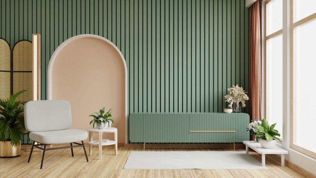A modern living room features a light grey armchair, a pale peach arched niche, a green cabinet, and plants against a green slatted wall.